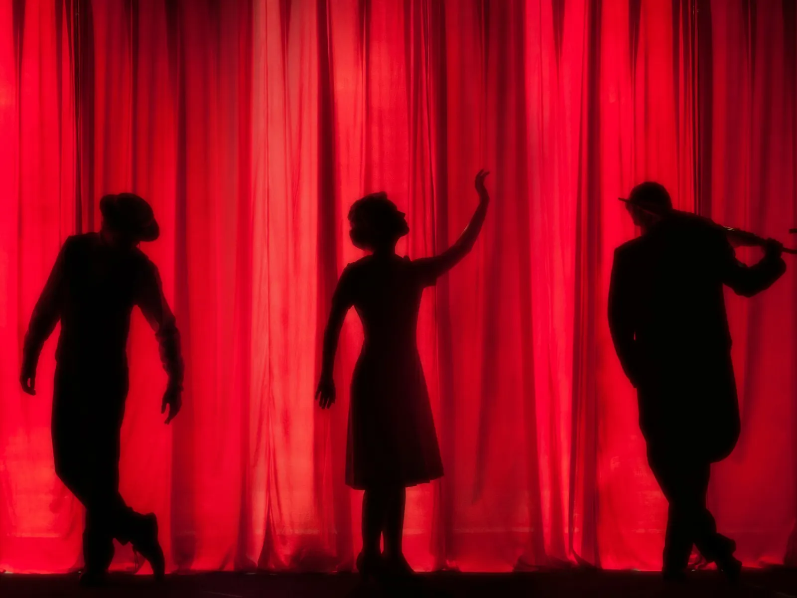 A red theatre curtain with three silhouetted figures in front of it